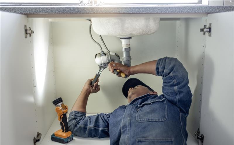 Plumber repairing pipes beneath a bathroom sink in San Ramon
