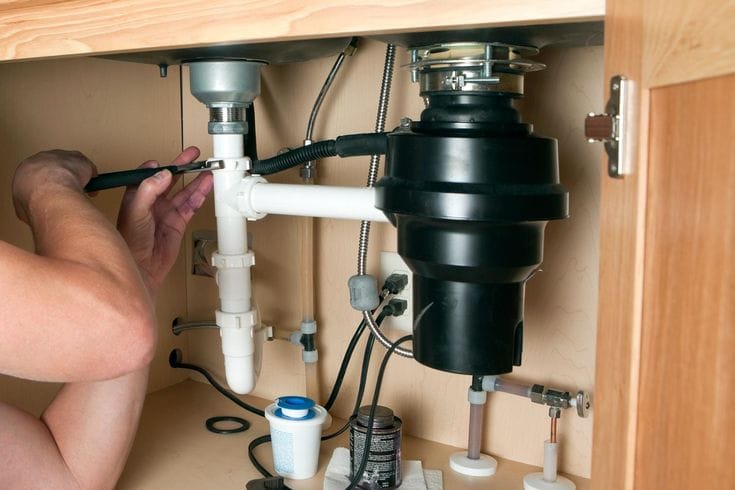 Plumber installing a garbage disposal beneath a kitchen sink in San Ramon