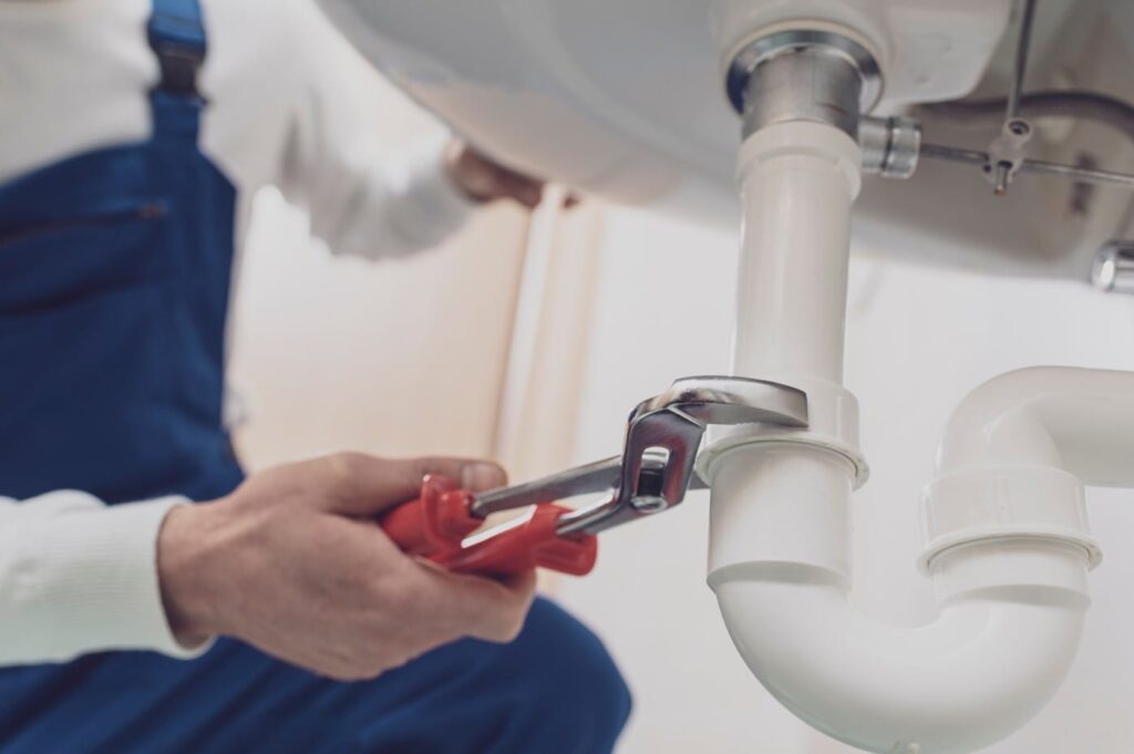 Plumber repairing a white drain pipe beneath a sink in San Ramon