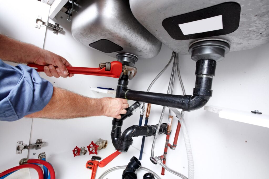 Plumber repairing drain pipes beneath a kitchen sink in San Ramon